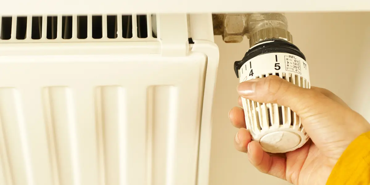 Main réglant le robinet thermostatique d'un radiateur